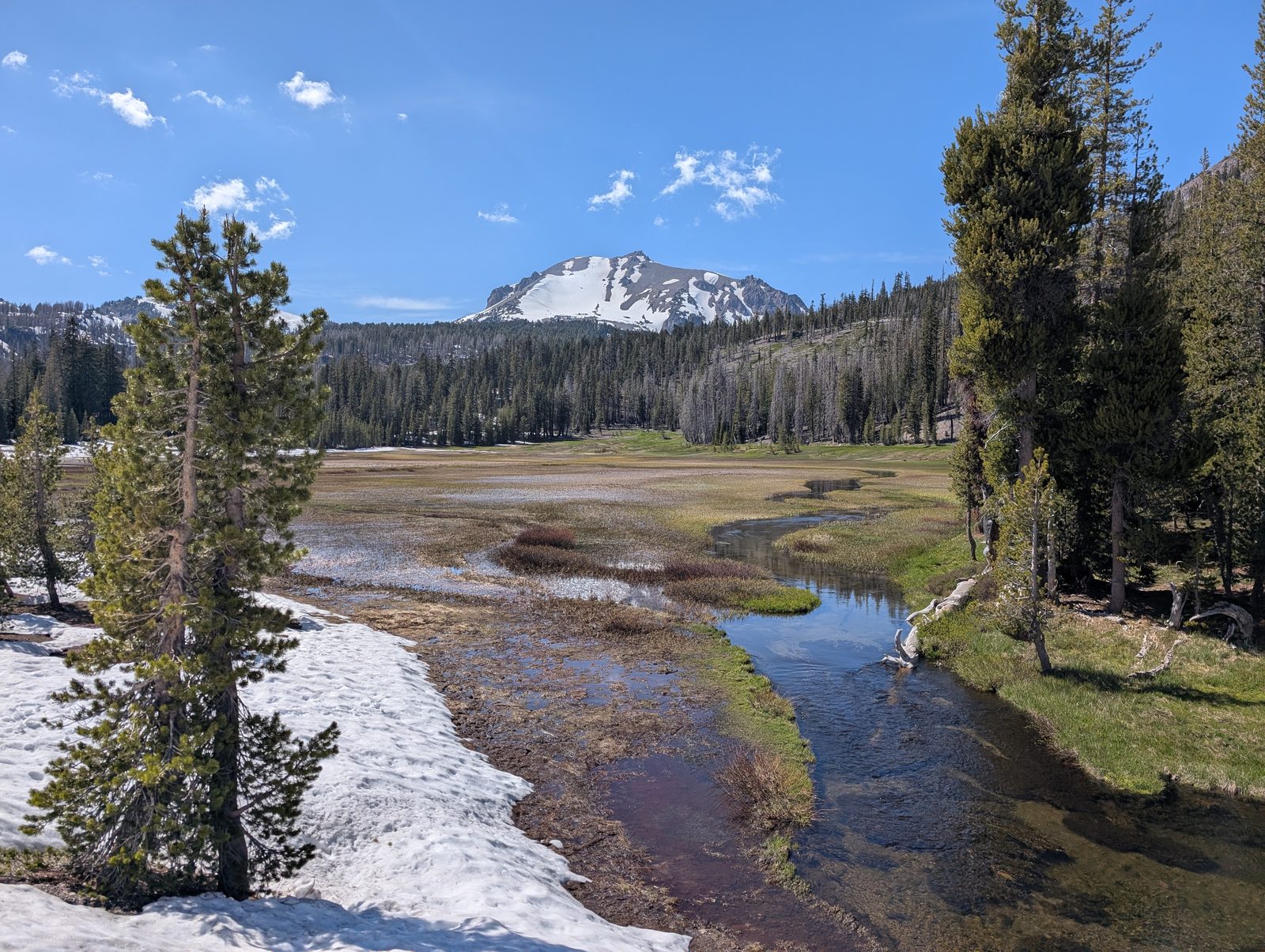 A stream winding through a snowmelt meadow with Lassen Peak rising in the distance
