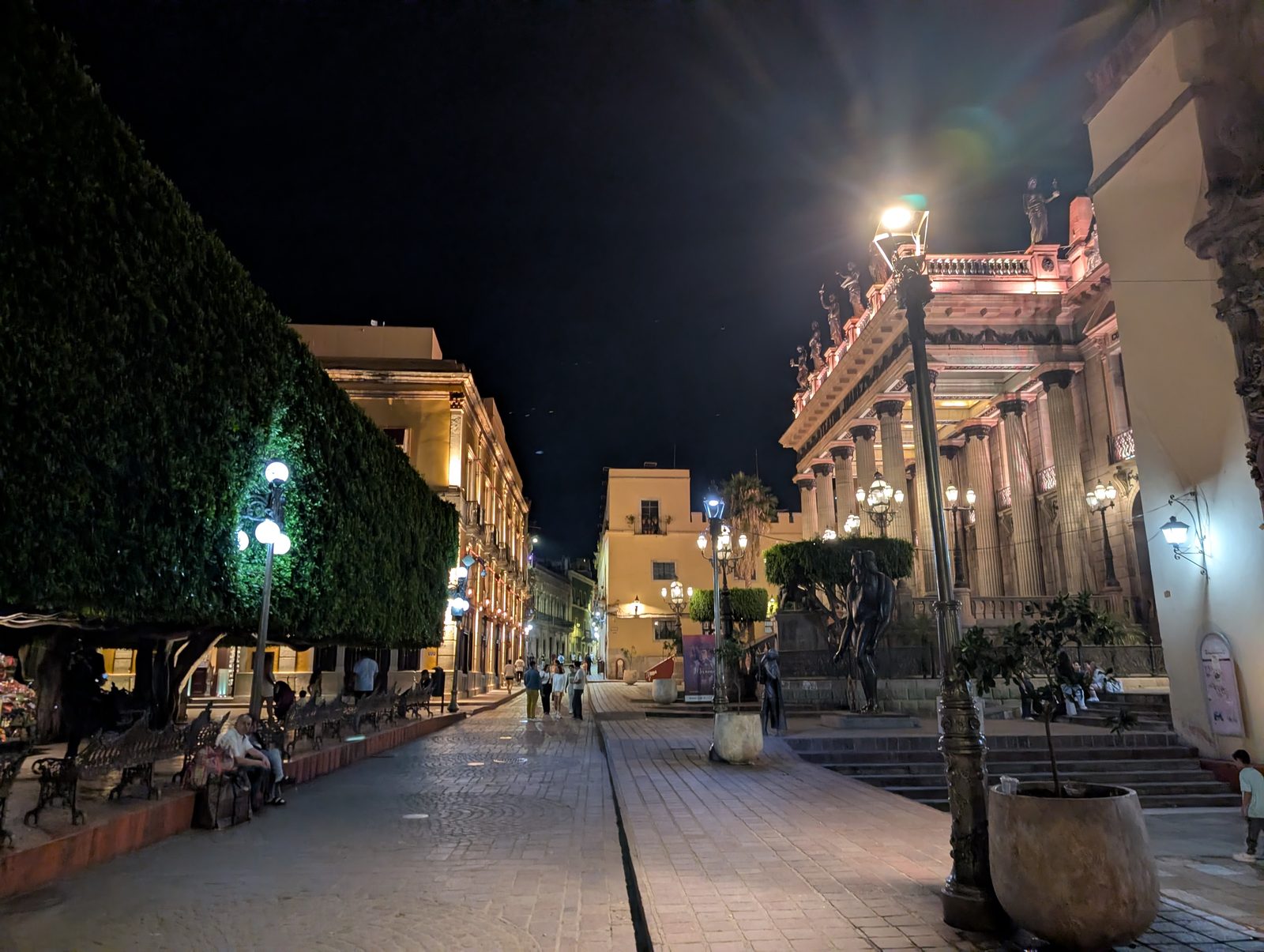 A plaza in front of Teatro Juárez lit up at night, with people strolling by